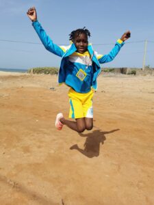 A young girl jumping in the air on top of a dirt field.
