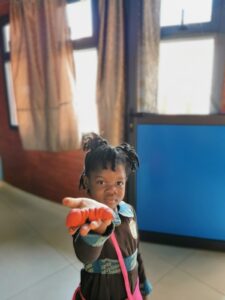 A young girl holding up an orange in her hand.