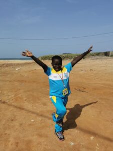 A man in blue and yellow shirt standing on dirt.