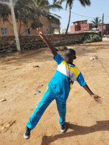 A person in blue and yellow shirt standing on dirt field.