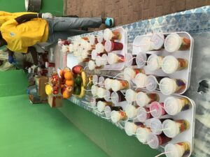 A table with many cups of juice and fruit.