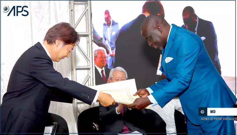 Two men in suits are exchanging a paper.